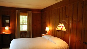 Een kamer met houten lambrisering, een bed, twee bedlampen, een raam met gordijnen en een spiegel aan de muur.