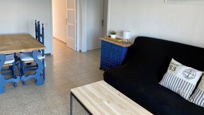 Huoneessa on puinen ruokapöytä, siniset tuolit, musta sohva, sininen kaappi ja seinällä oleva kehystetty kuva.