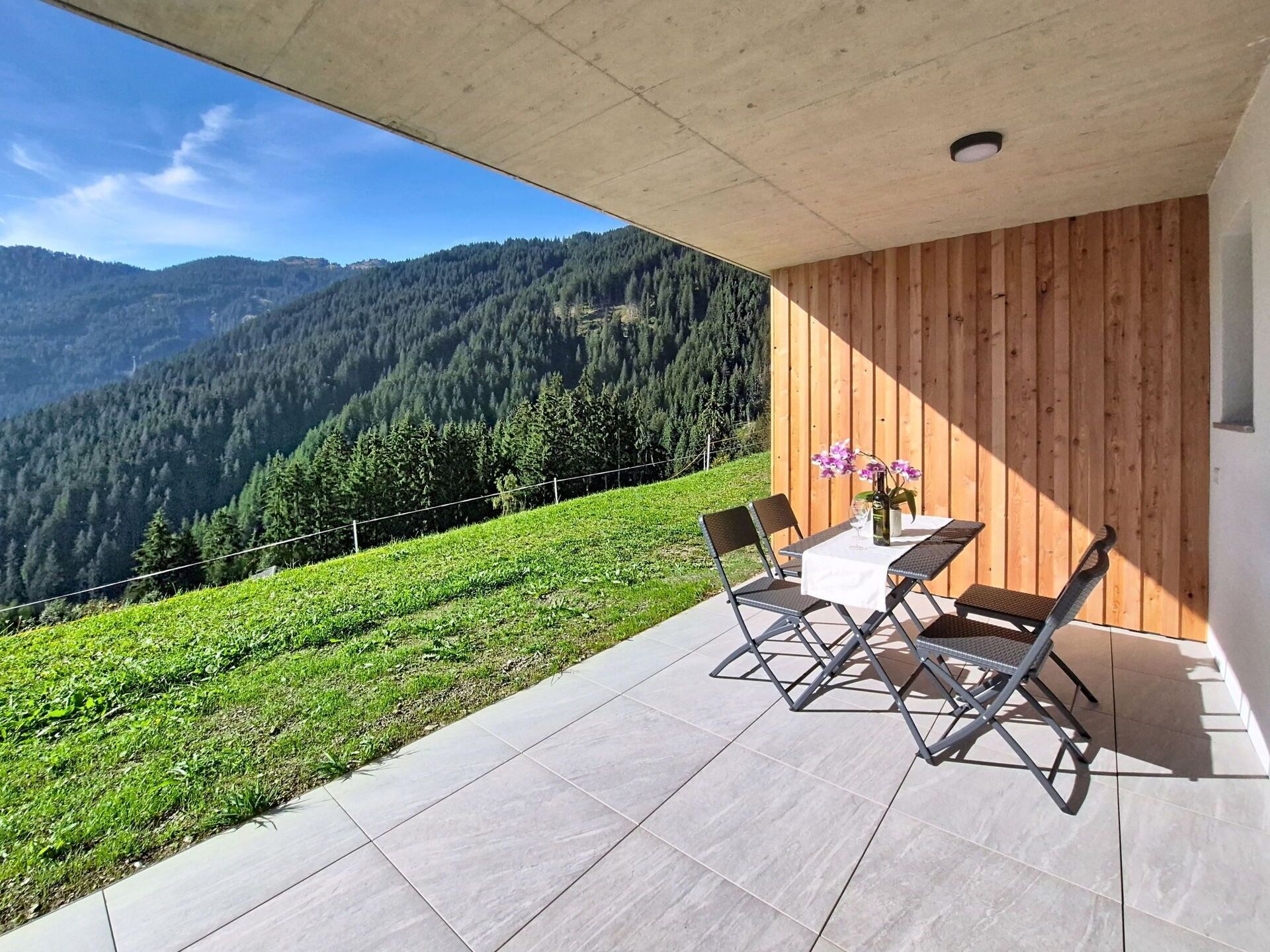 A balcony with a table and chairs, overlooking a mountainous landscape.