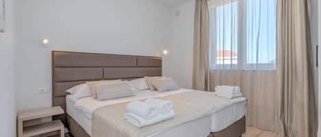 A double bed with a headboard, bedside tables, and a window with curtains.