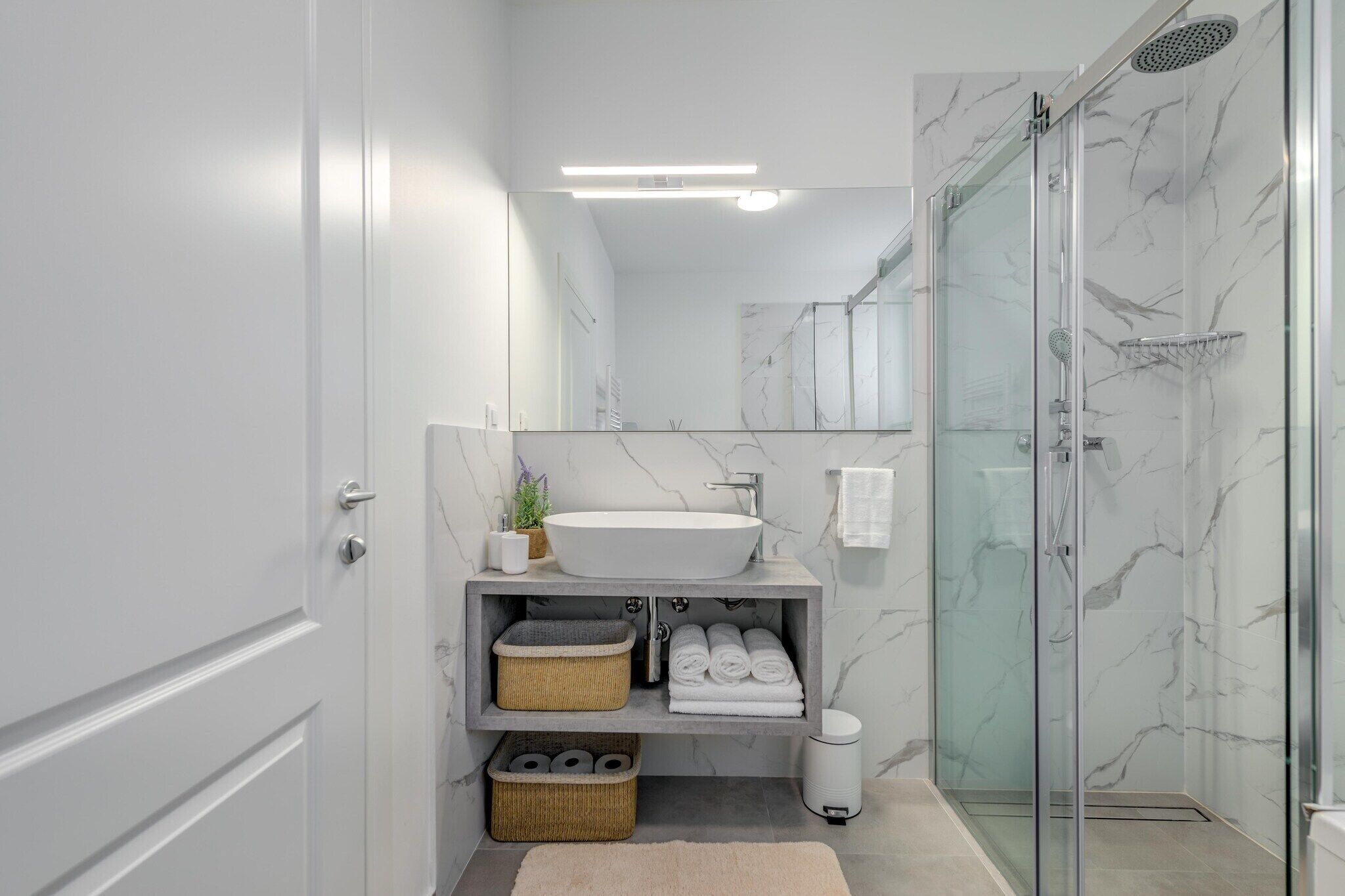 Une salle de bain moderne avec une douche en verre, un lavabo blanc et des murs en marbre.