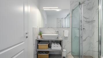 Une salle de bain moderne avec une douche en verre, un lavabo blanc et des murs en marbre.