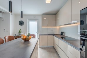 A modern kitchen with a long countertop, cabinets, and a dining area with chairs and a table. - Modern Escape Villa with Private Pool (Solin)