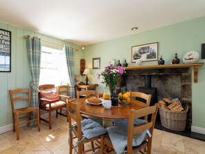 A dining area with a round table, chairs, a fireplace, and a window with curtains.