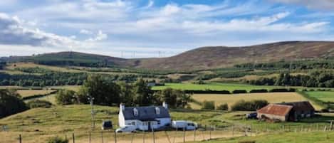 A rural landscape with rolling hills, a white house, and a fenced field.