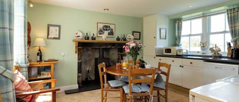 A cozy kitchen with a dining table, chairs, a fireplace, and a window with curtains.