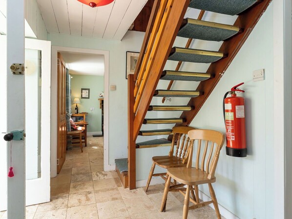 A staircase with a wooden handrail and carpeted steps, a fire extinguisher mounted on the wall, and a chair in the foreground.