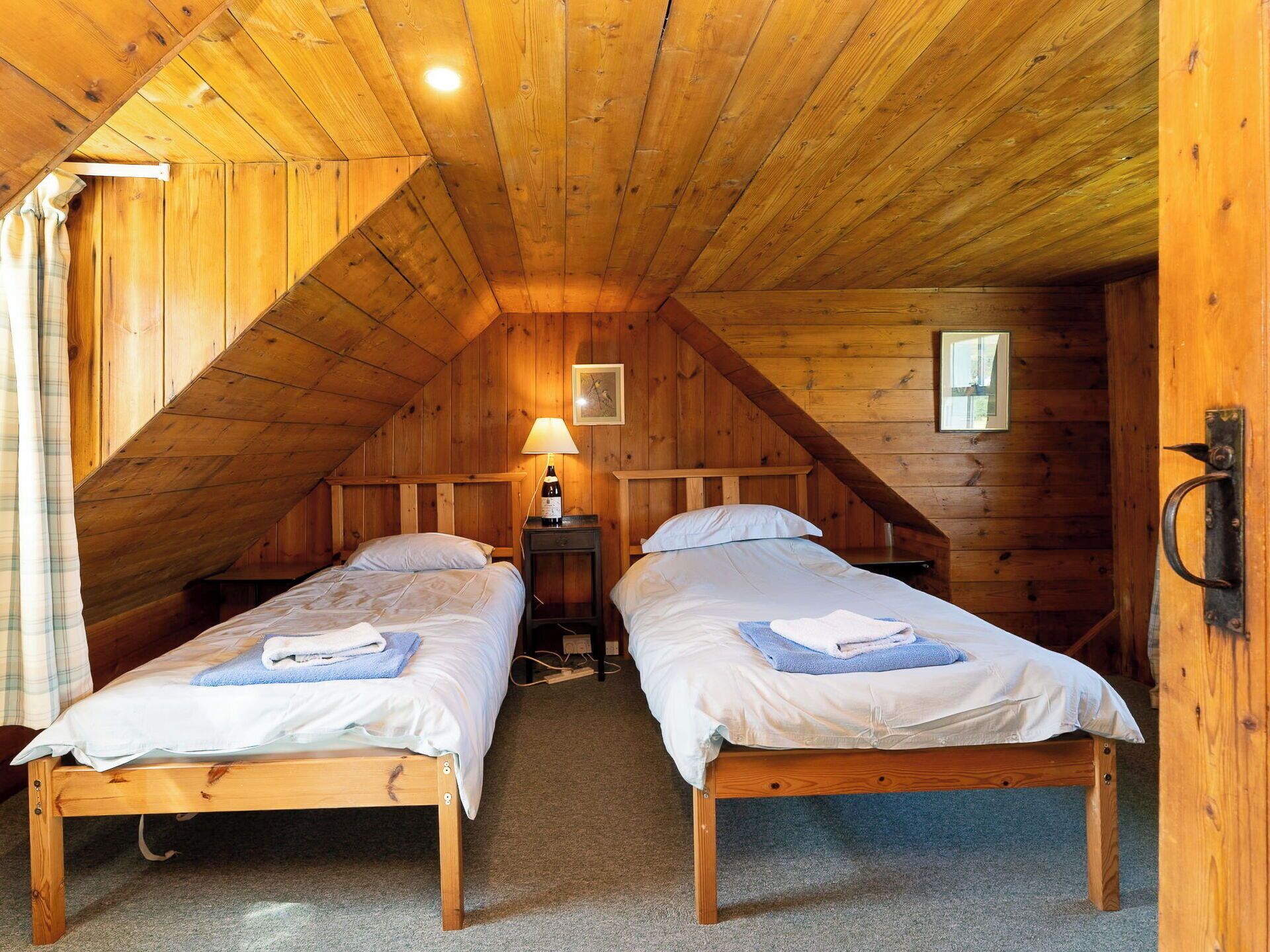 A room with two wooden beds, a lamp, and a framed picture on the wall.
