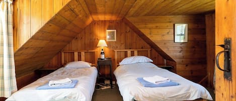 A room with two wooden beds, a lamp, and a framed picture on the wall.