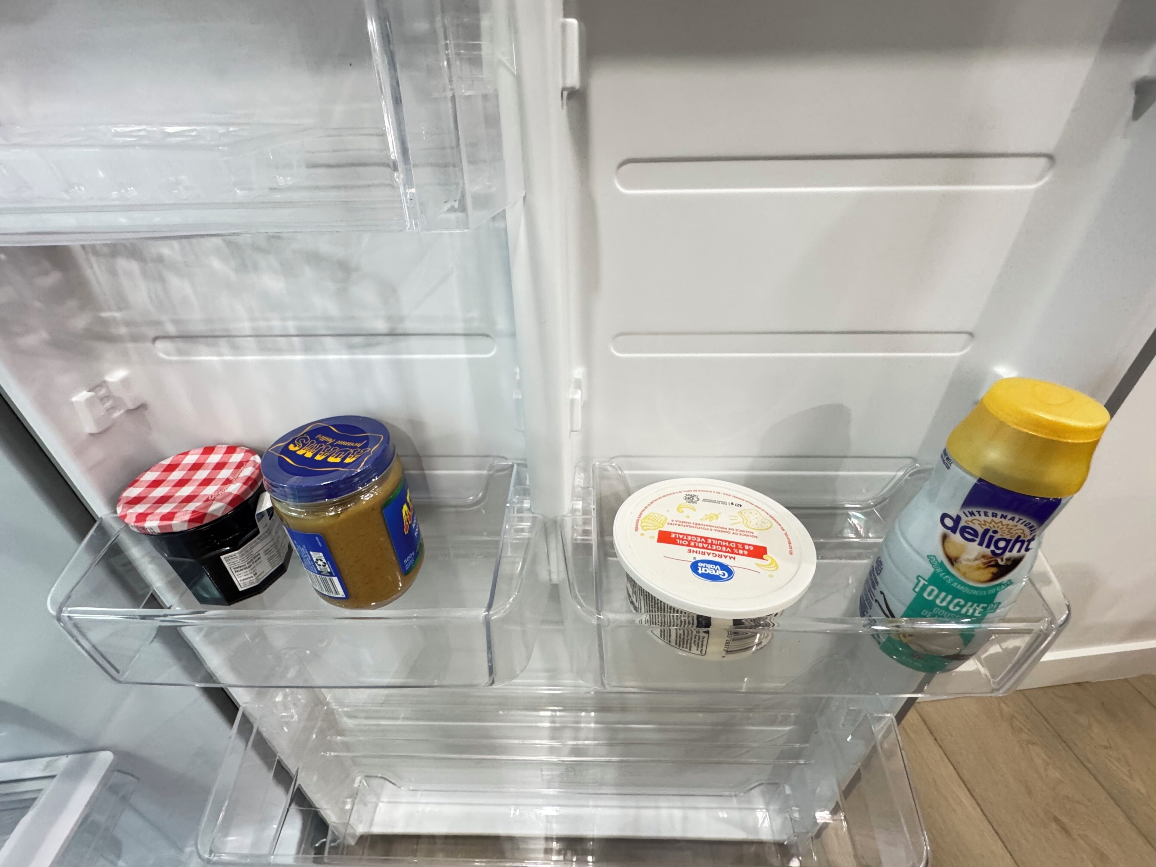 Een koelkast met transparante planken, gevuld met een pot pindakaas, een bakje yoghurt en een fles melk.