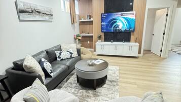 Ein modernes Wohnzimmer mit einem Ledersofa, grauen Sesseln, einem Couchtisch und einem flachbildfernseher, der an einer Holzwand befestigt ist.