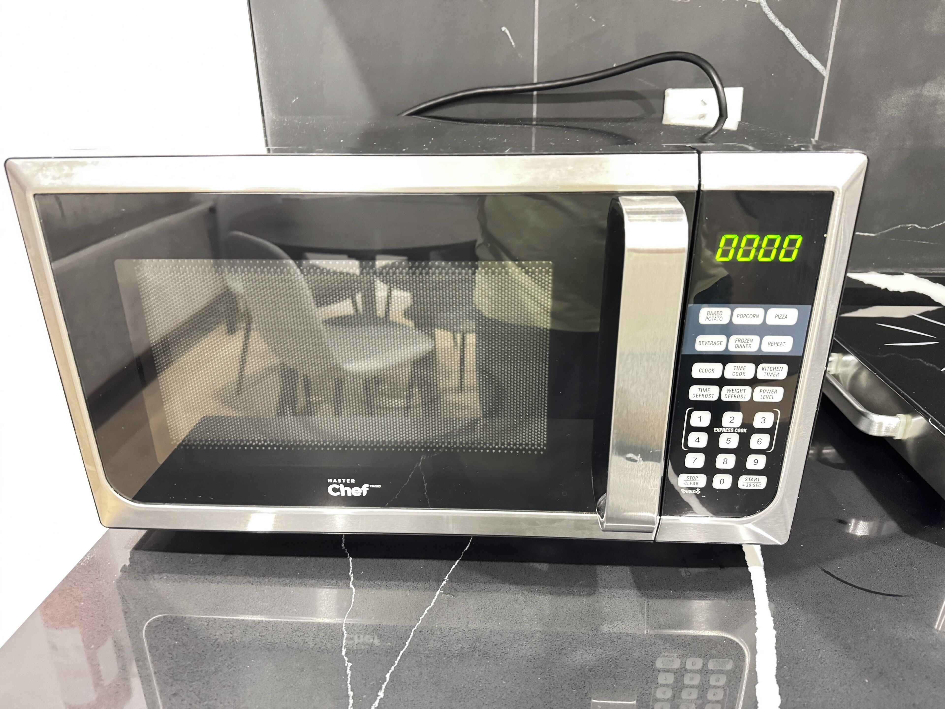 A microwave oven with a digital display, control panel, and a power cord plugged in.