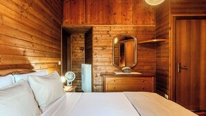 Una habitación de madera con una cama, un aparador, un espejo y una puerta.