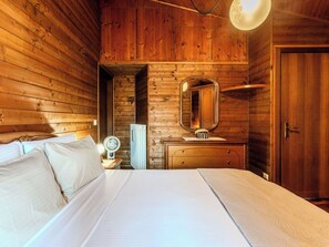 Une pièce en bois avec un lit, une commode, un miroir et une porte.