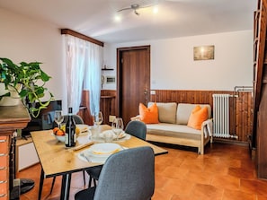 Ein Essbereich mit Tisch für zwei Personen, einer Couch mit Kissen, einer Topfpflanze und einer Holztür.