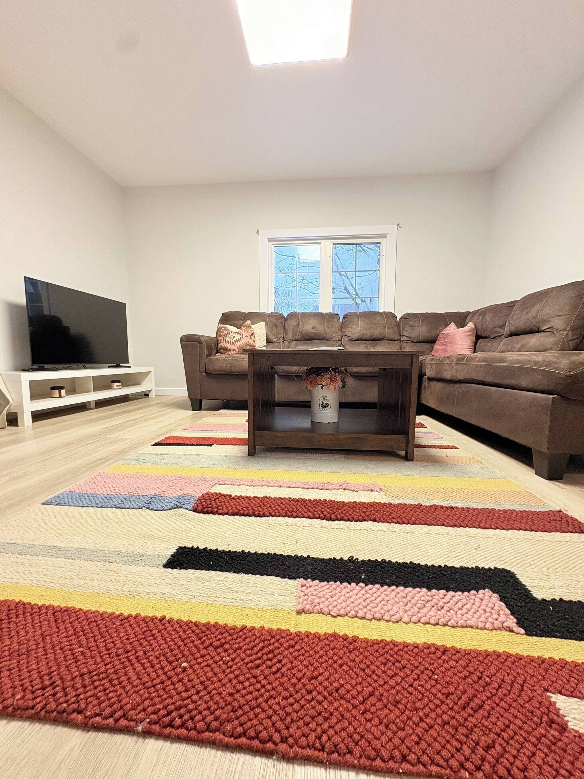 A living room with a flat-screen TV, two sofas, a coffee table, and a colorful rug.