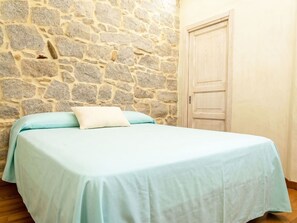 Ein Zimmer mit einer Steinsäule, einer Holztür und einem Bett mit heller Bettdecke.