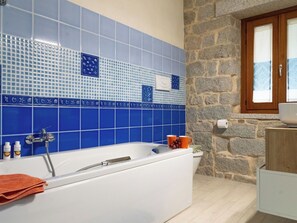 Ein Badezimmer mit Badewanne, einer Steinwand und einem Fenster.