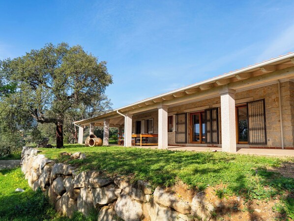 Ein modernes Haus mit Natursteinfassade, großen Fenstern und einer überdachten Terrasse.