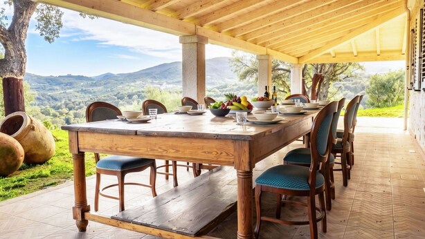 Un espacio de comedor techado con una mesa de madera, sillas y vistas al campo.