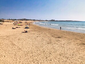 Ein breiter Sandstrand mit Sonnenschirmen und Menschen.