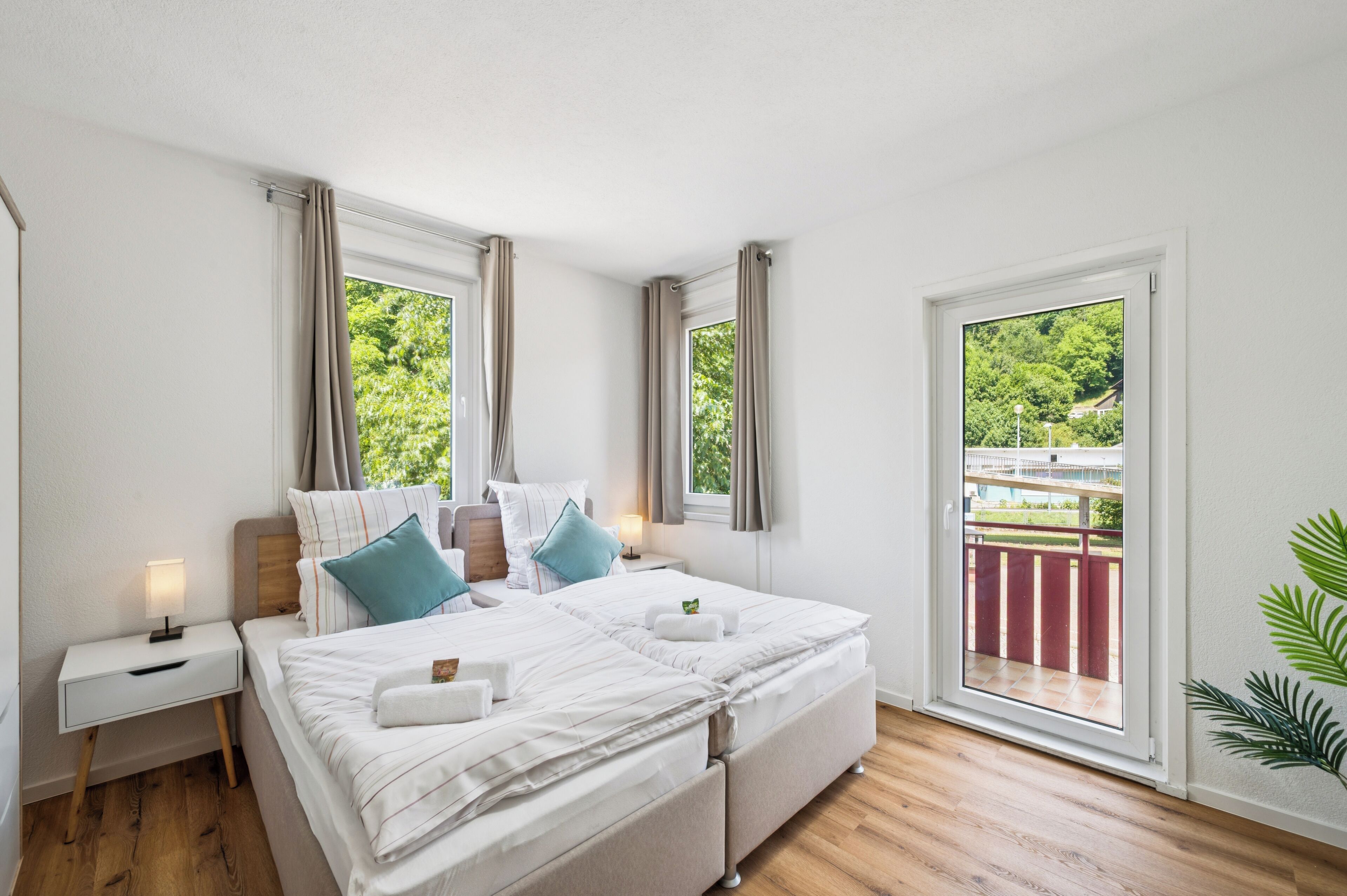 A bedroom with a bed, bedside tables, curtains, and a view of greenery outside.