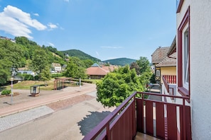 Un quartier résidentiel avec un balcon rouge, une allée couverte et une vue sur une colline où se trouvent des maisons.