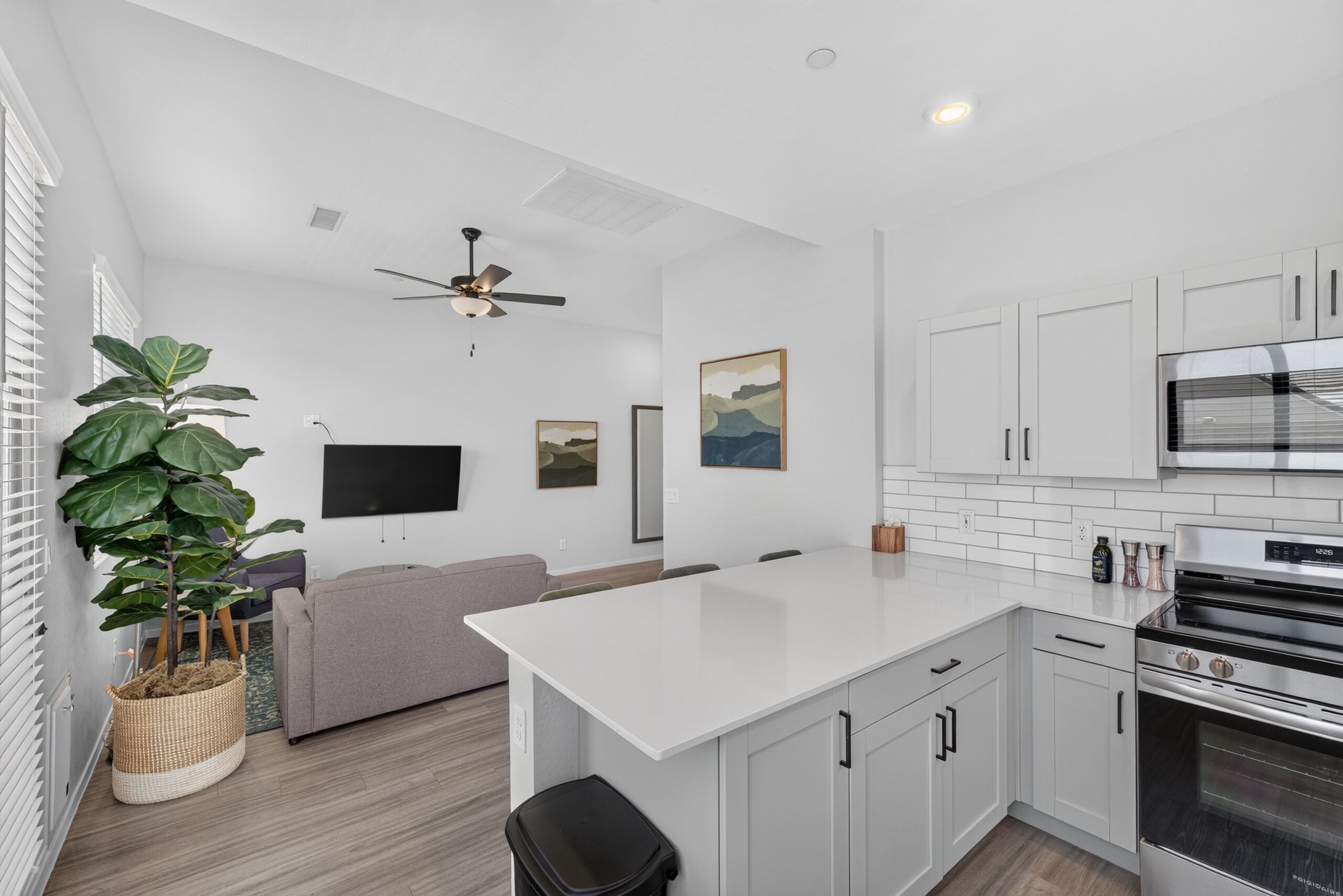 A modern kitchen with white cabinets, a large island, a built-in oven, and a ceiling fan.