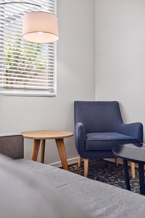 A room with a blue armchair, a small round table, a sofa, and a hanging lamp.