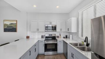 A modern kitchen with white cabinets, stainless steel appliances, and a wooden floor.