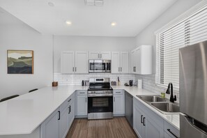 A modern kitchen with white cabinets, stainless steel appliances, and a wooden floor.
