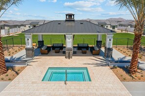 A pool area with a covered seating area, a pool, and a view of residential buildings in the background.