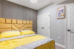 A bedroom with a bed, a headboard, a door, and a wall-mounted picture. - An Elegant & Comfy 2- Bedroom 2-Bathroom Ensuite (Calgary)