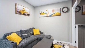 Una sala de estar con un sofá modular gris, cojines amarillos, una mesa de centro oscura y obras de arte en las paredes.