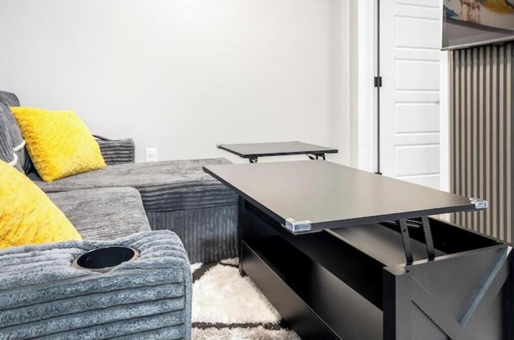 A modern living room with a grey sofa, yellow cushions, a black coffee table, and a white door in the background.