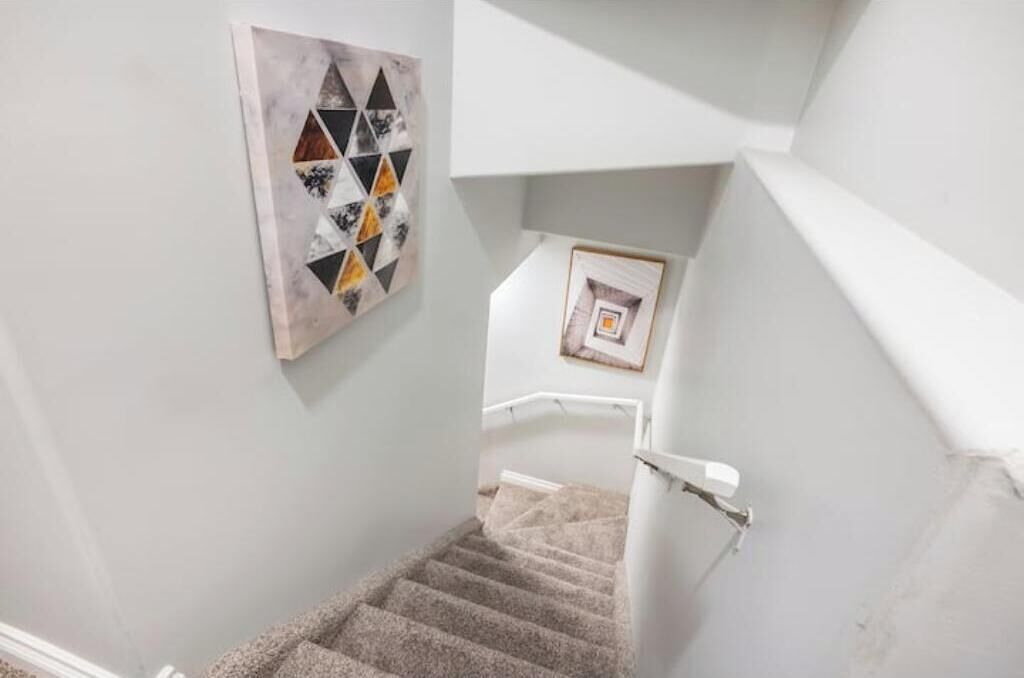 A staircase with a carpeted handrail, a geometric wall art piece, and a framed picture on the wall.