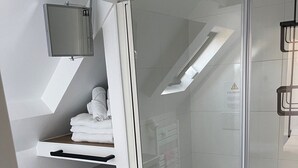 Een moderne badkamer met een douchecabine van glas, een bevestigde televisie en netjes opgevouwen handdoeken op een plank.
