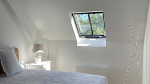 Een slaapkamer met dakraam, een bed met een geborduurd sprei, een nachtkastje met lamp en een vloerlamp.