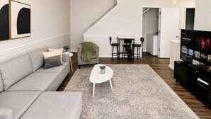 Ett vardagsrum med en soffa, ett soffbord, en tv och en matplats med stolar.