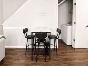 Un comedor con una mesa y cuatro sillas, una pared blanca con un termostato y suelo de madera.