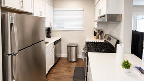 Una cocina moderna con electrodomésticos de acero inoxidable, armarios blancos, una estufa a gas y un pequeño cubo de basura.
