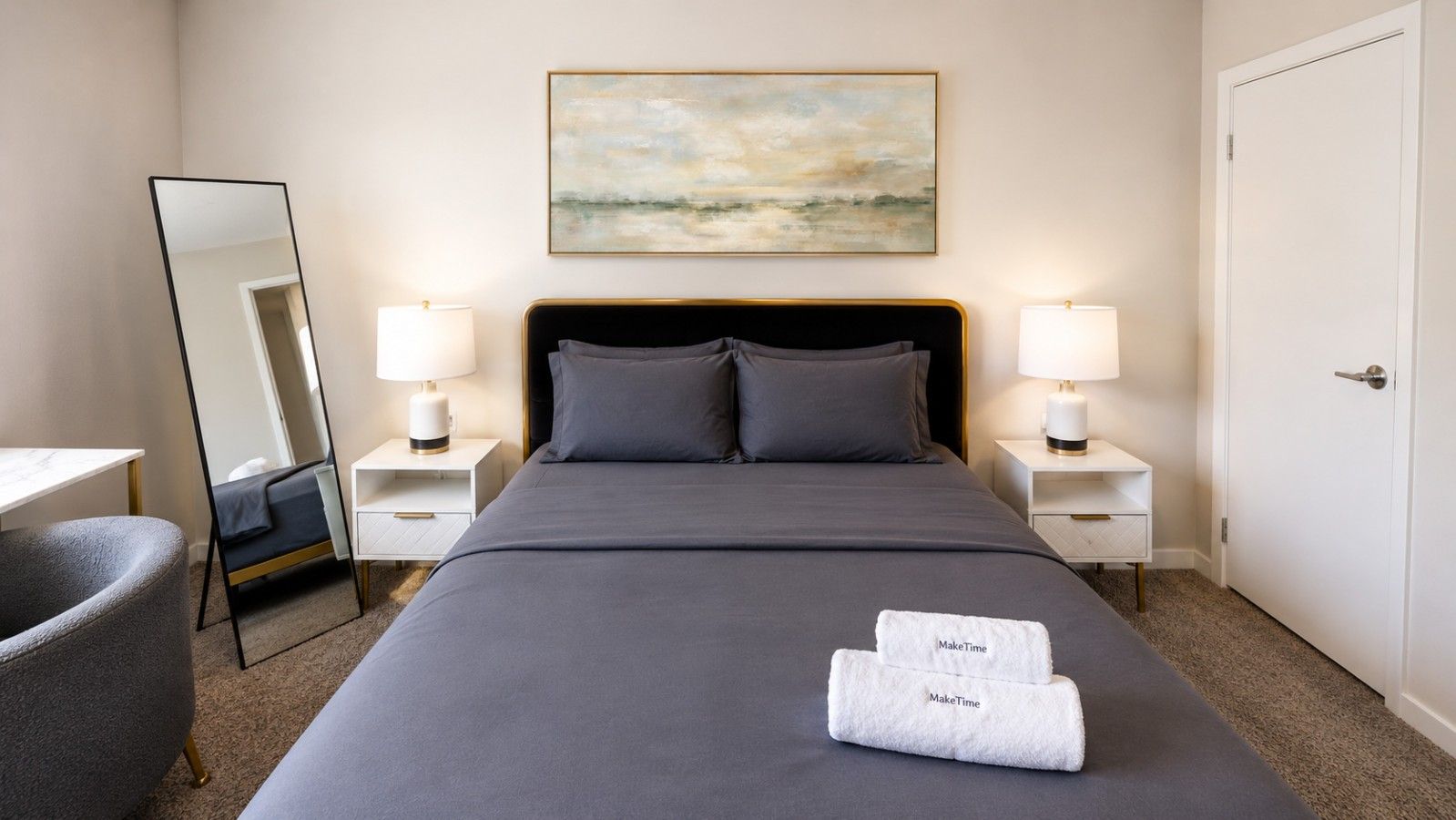 Ein Hotelzimmer mit einem Bett, zwei Nachttischen mit Lampen, einem Sessel und einem großen Spiegel, sowie einem Bild an der Wand.