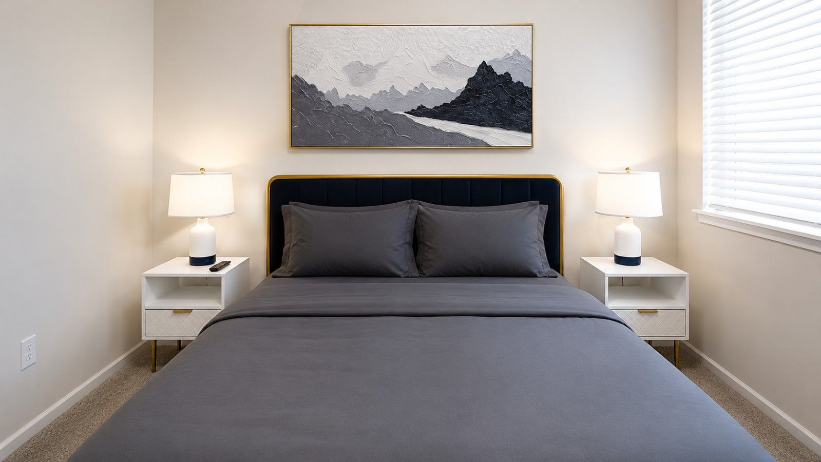 A bedroom with a bed, two bedside tables, lamps, and a framed picture on the wall.