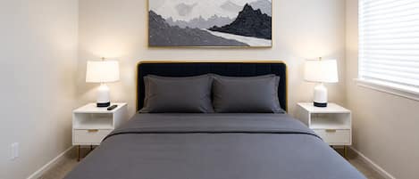 A bedroom with a bed, two bedside tables, lamps, and a framed picture on the wall.
