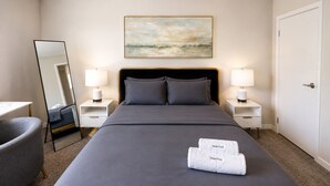 Ett hotellrum med en säng, två sängbord med lampor, en stol, en stor spegel och en tavla på väggen.