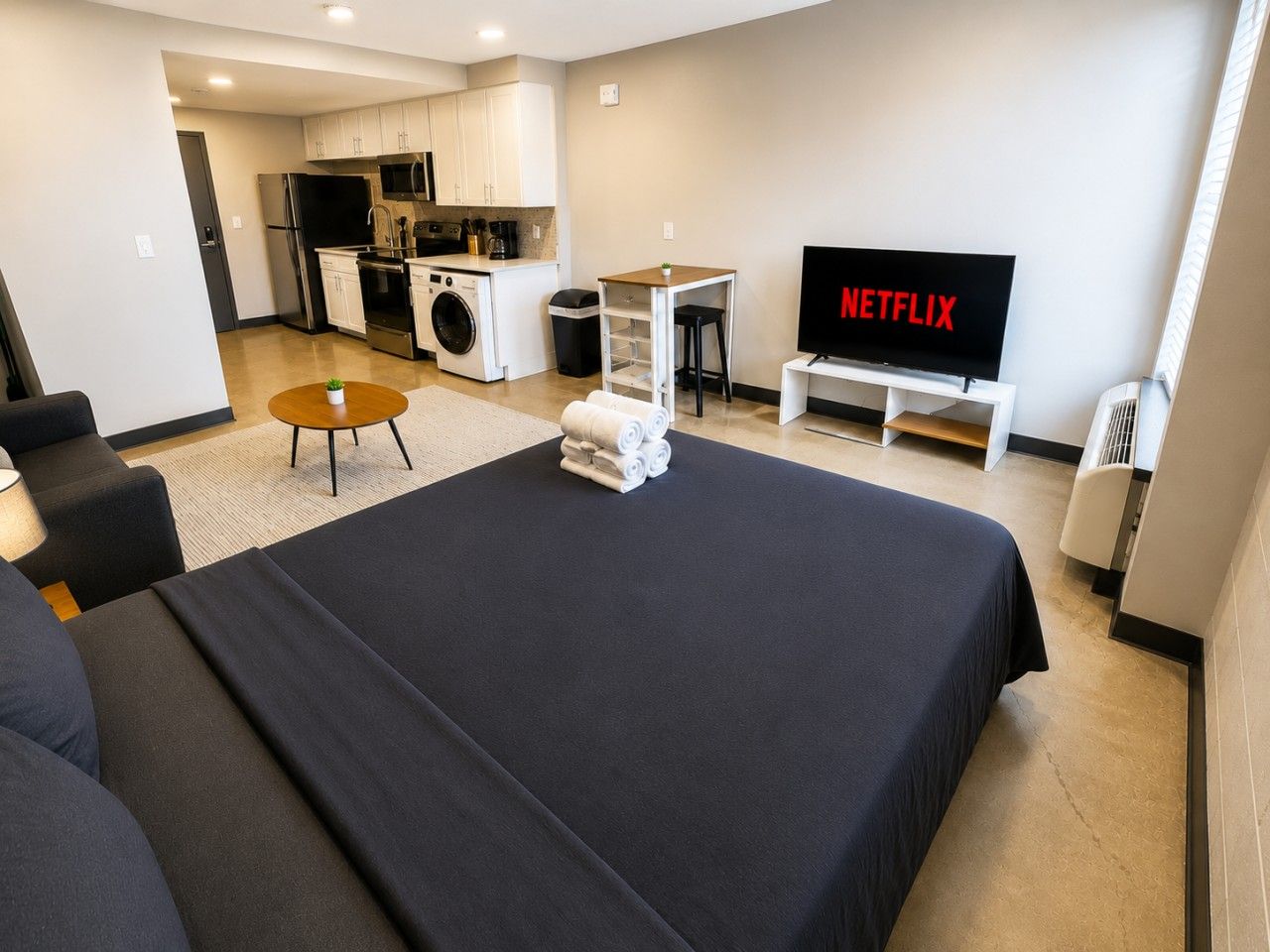 Camera d'albergo moderna con un letto grande, un piccolo tavolo rotondo, una televisione, angolo cottura e lavanderia.
