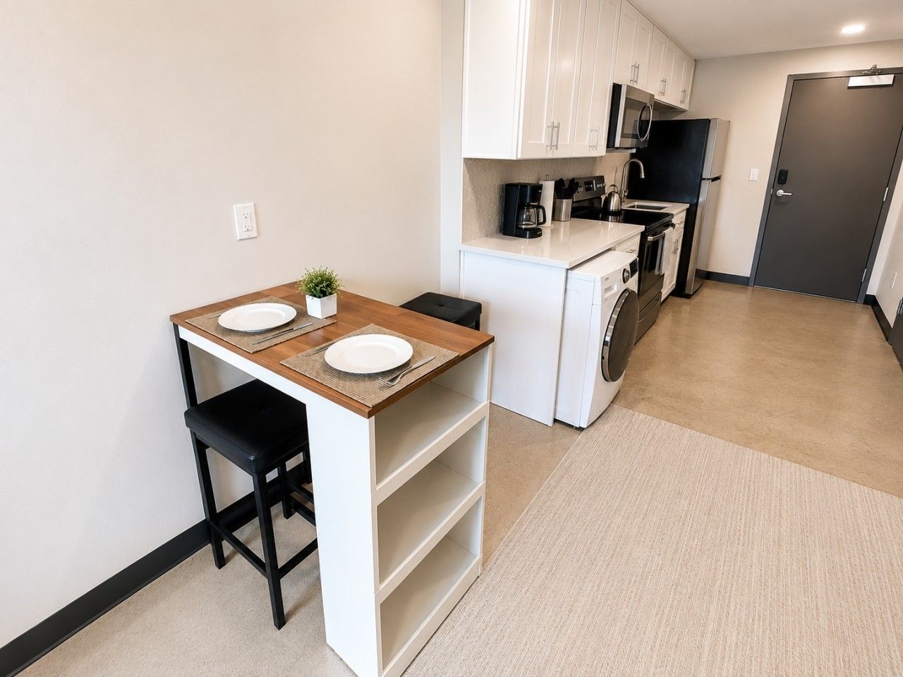 A compact kitchen with a small dining area, a washing machine, and a door.