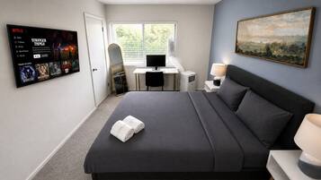 Una habitación de hotel con cama, escritorio, computadora, televisor y un cuadro en la pared.