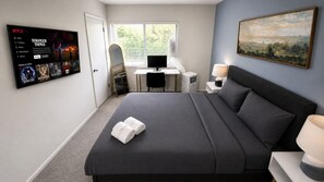 A hotel room with a bed, desk, computer, TV, and a painting on the wall.