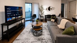 A living room with a flat-screen TV, a coffee table, a sofa, and a dining area with chairs. - Iron City Retreat | Modern 2BR Stay #4 (Birmingham)